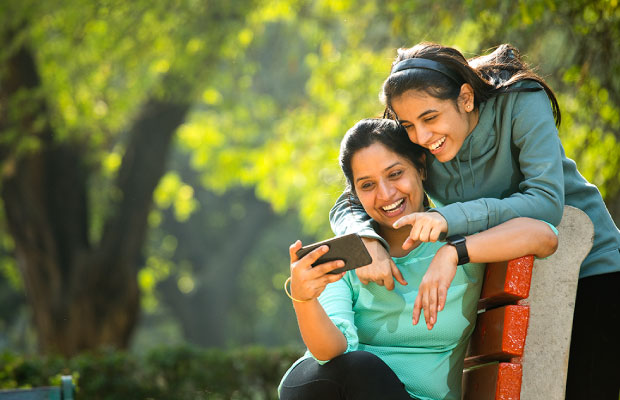 Image of mother and daughter sitting on a park bench and looking at a mobile phone